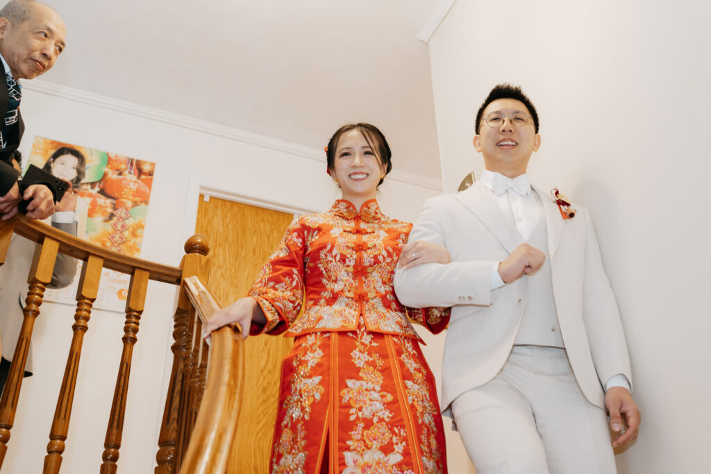 Chinese bride and groom going down the stairs under the eye of the bride's father. The bride is wearing a red Qun Kwa dress. 
